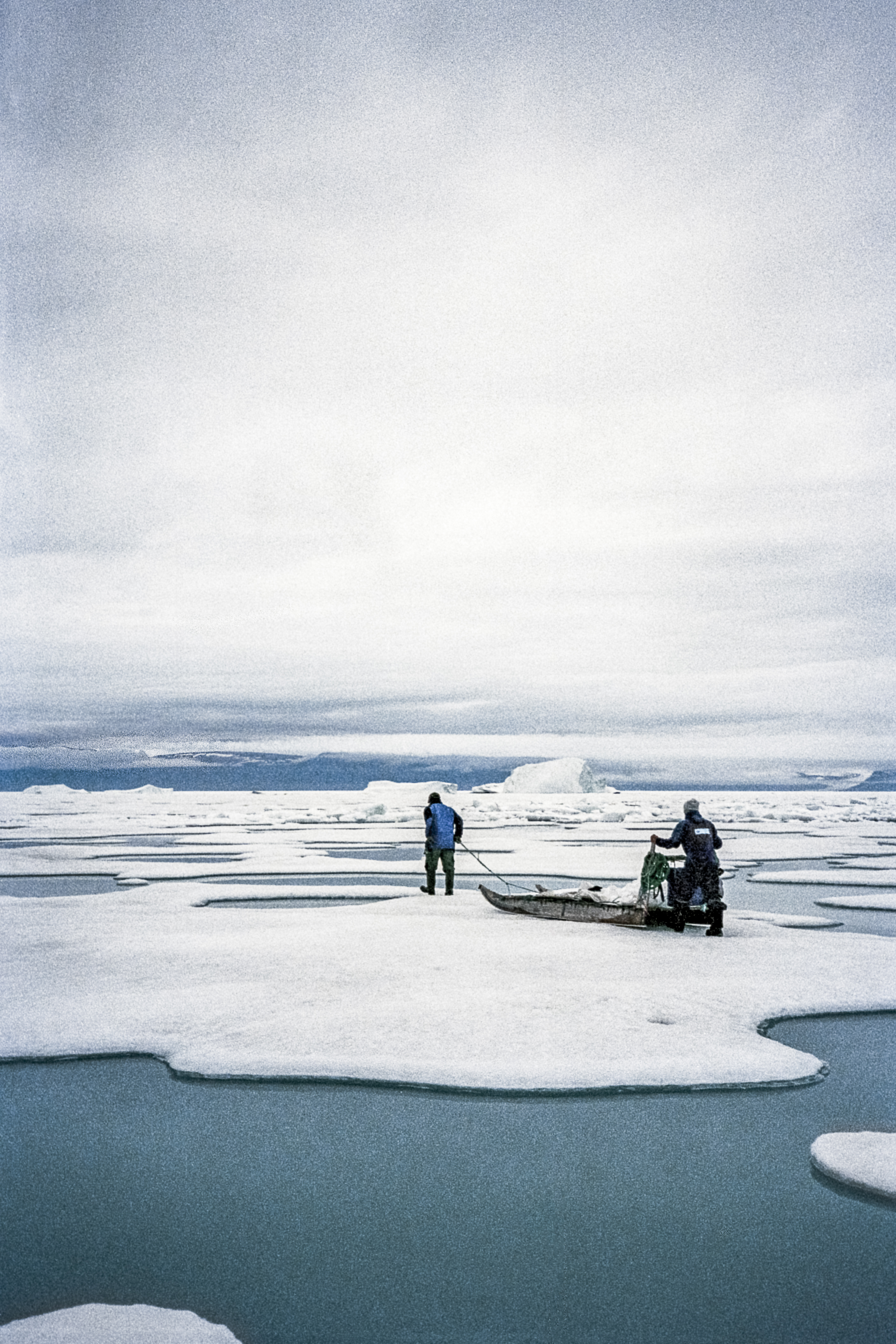 Inuuteq Storch - Two people standing on planks of ice with a camera on the sea