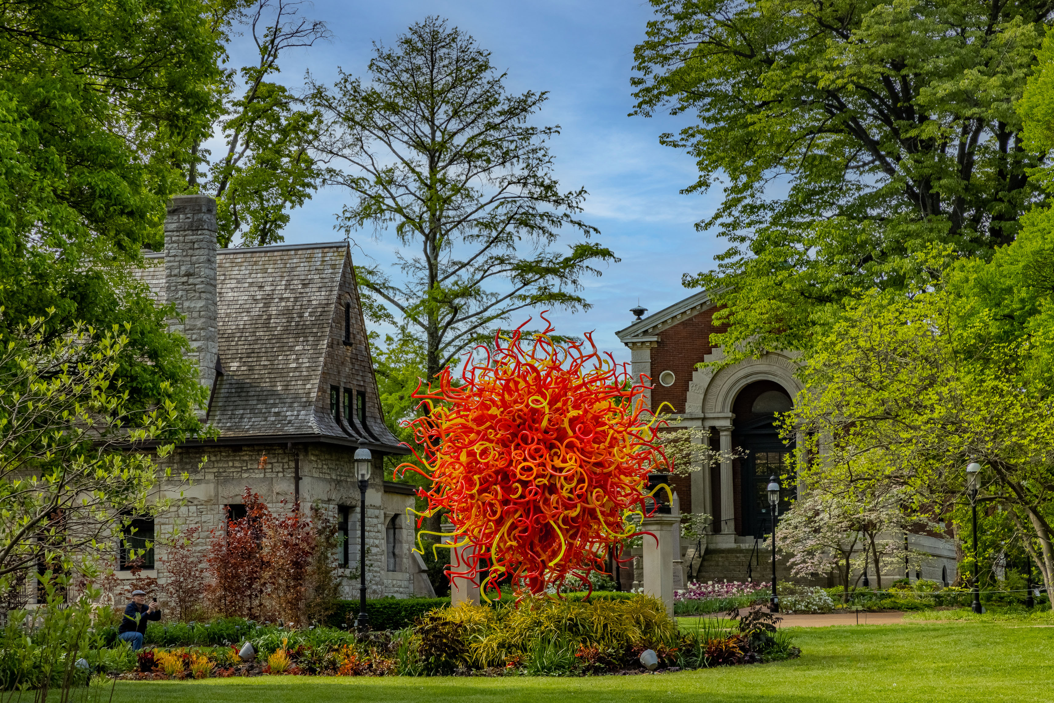 Chihuly - orange and red venetian glass sculpture in a garden next to a stone house
