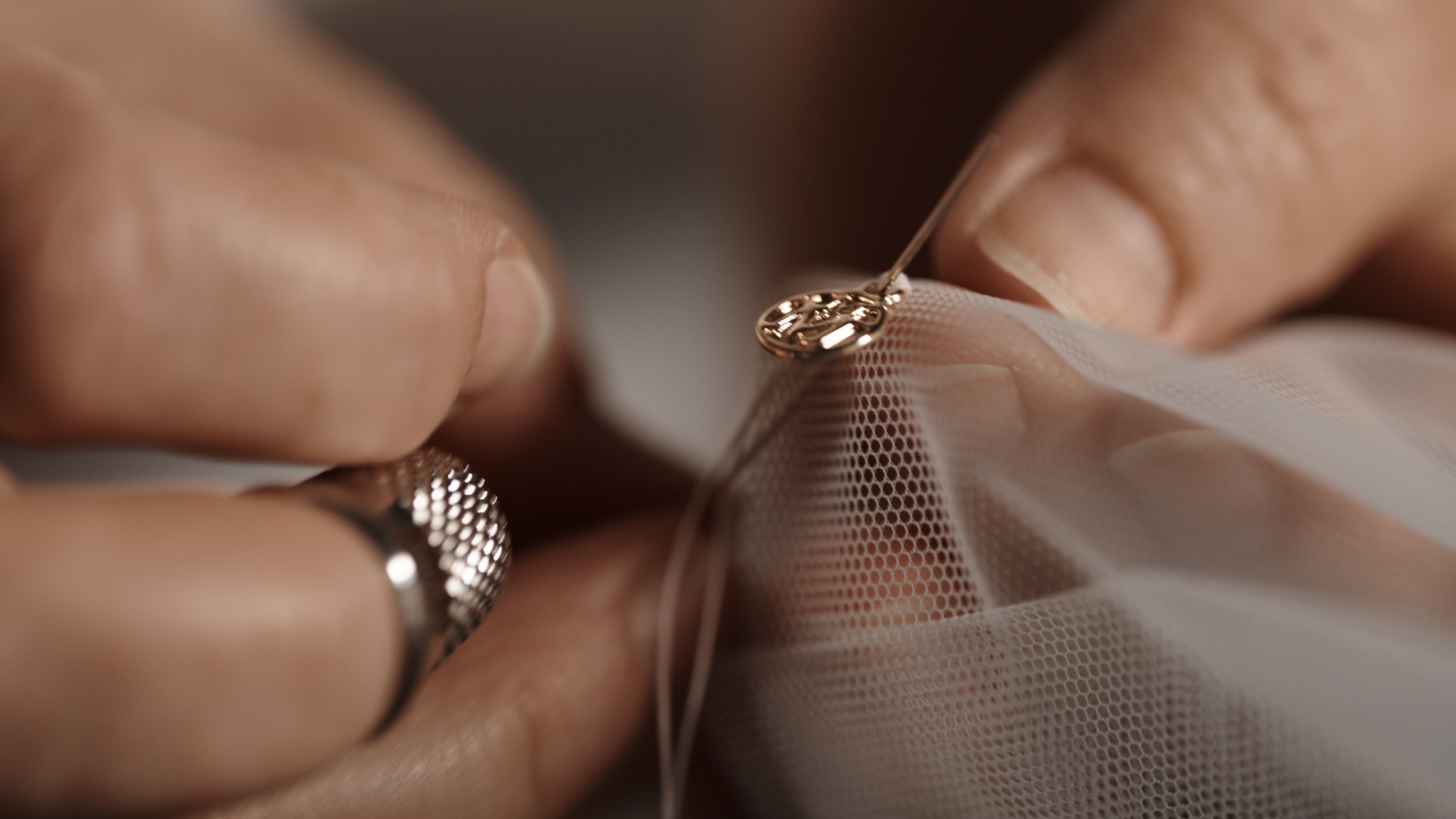 Maison Michel- A persons hand threading a charm through mesh material with a needle