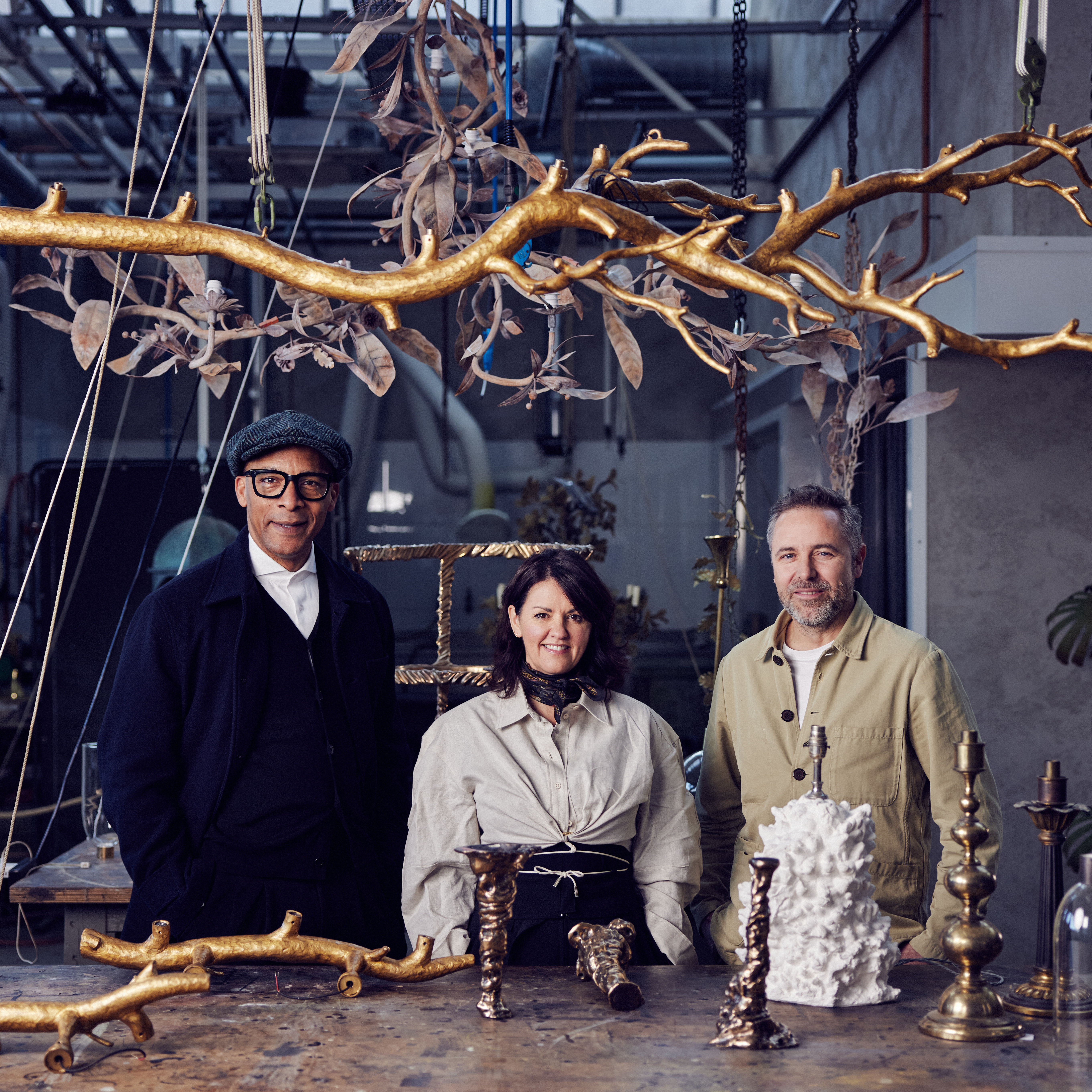 Cox London - three people standing by a table with gold objects around and above them