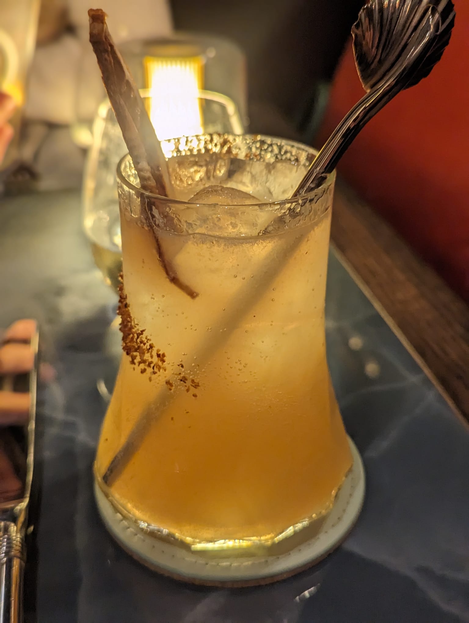 VATAVARAN - an orange cocktail in a glass with tajin on the side