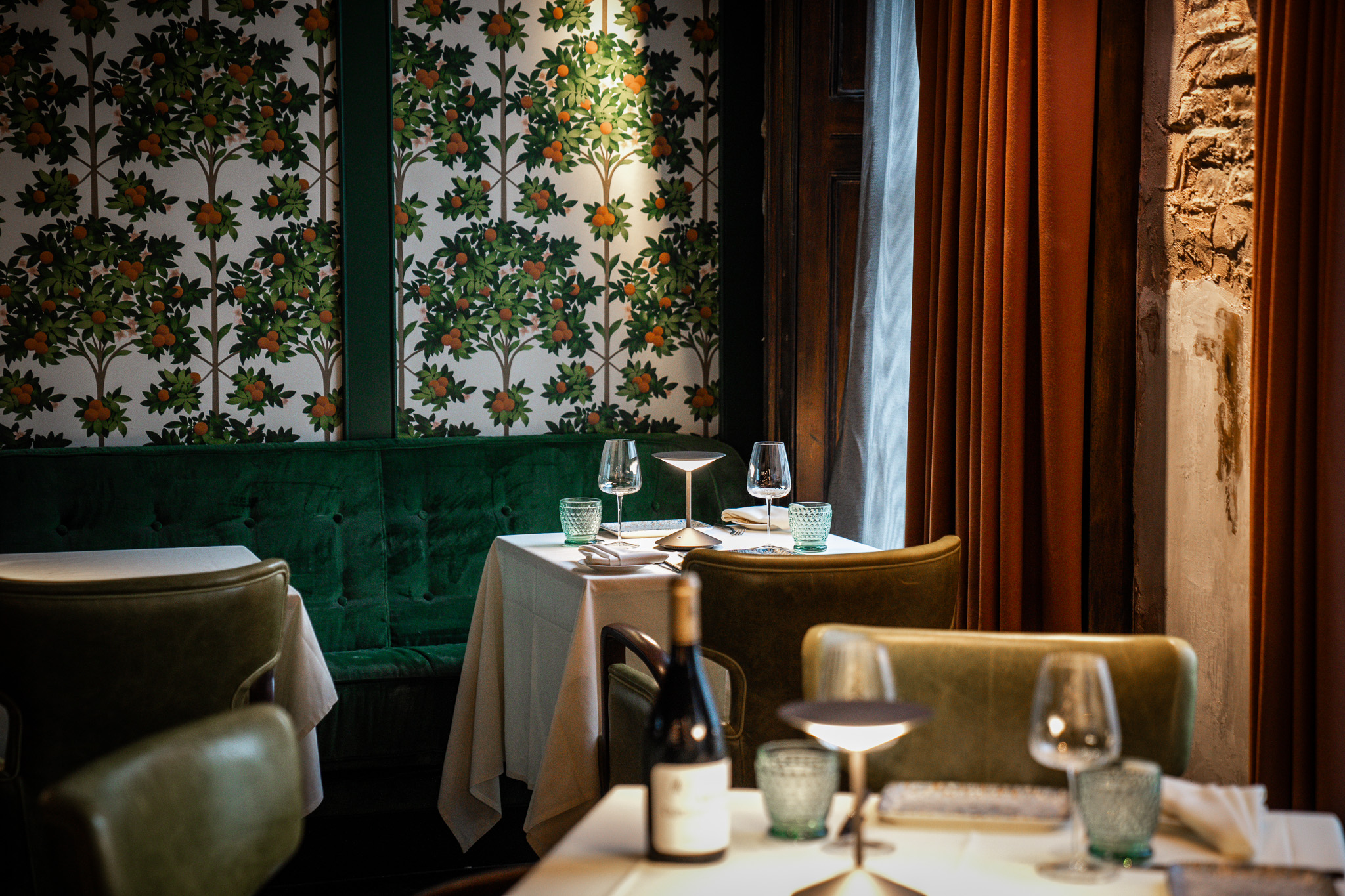 VATAVARAN- a dining area with tableclothed tabels and wine glasses, green decorative wallpaper