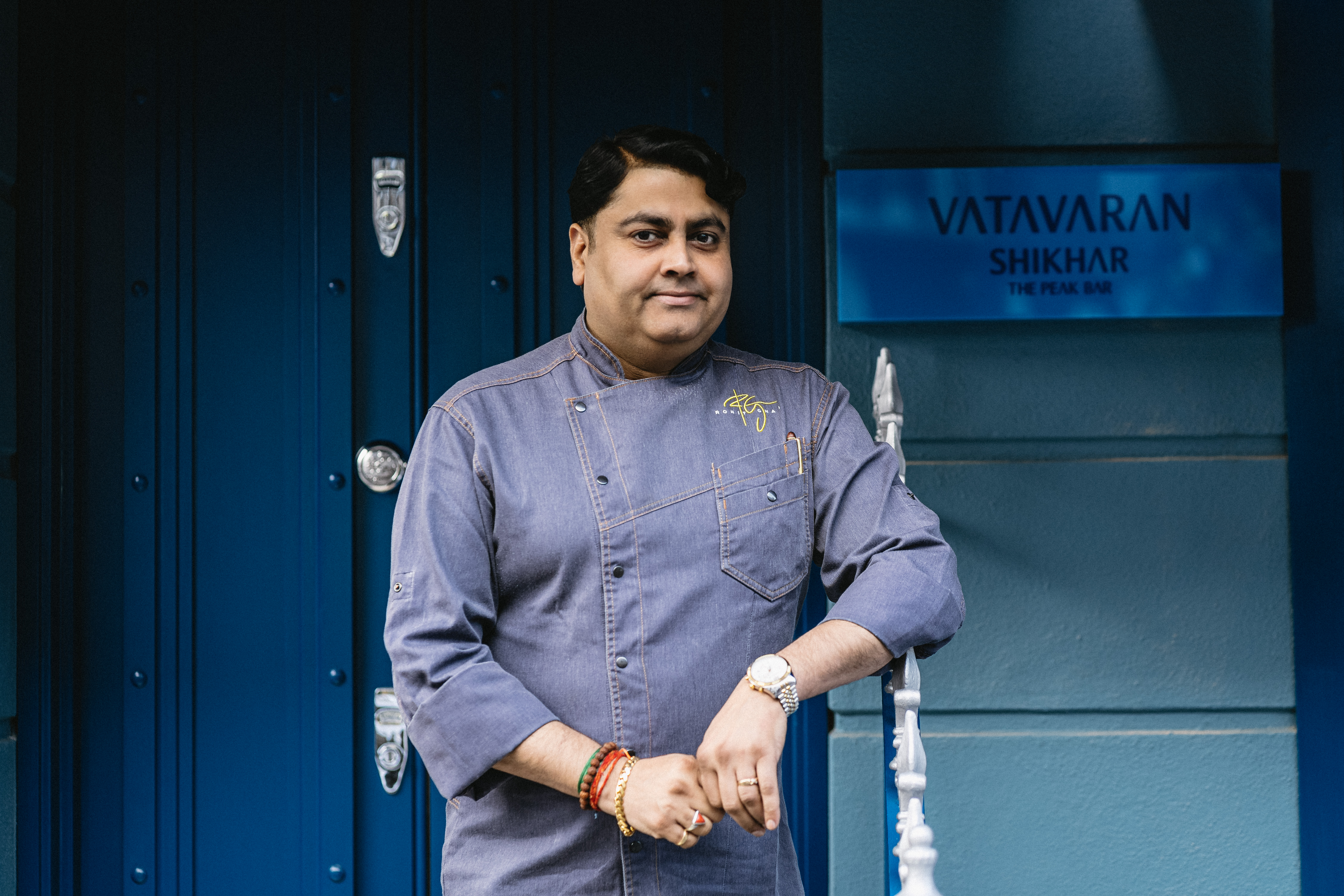 VATAVARAN - chef ghai wearing a blue chef jacket infront of the blue front door of Vatavaran