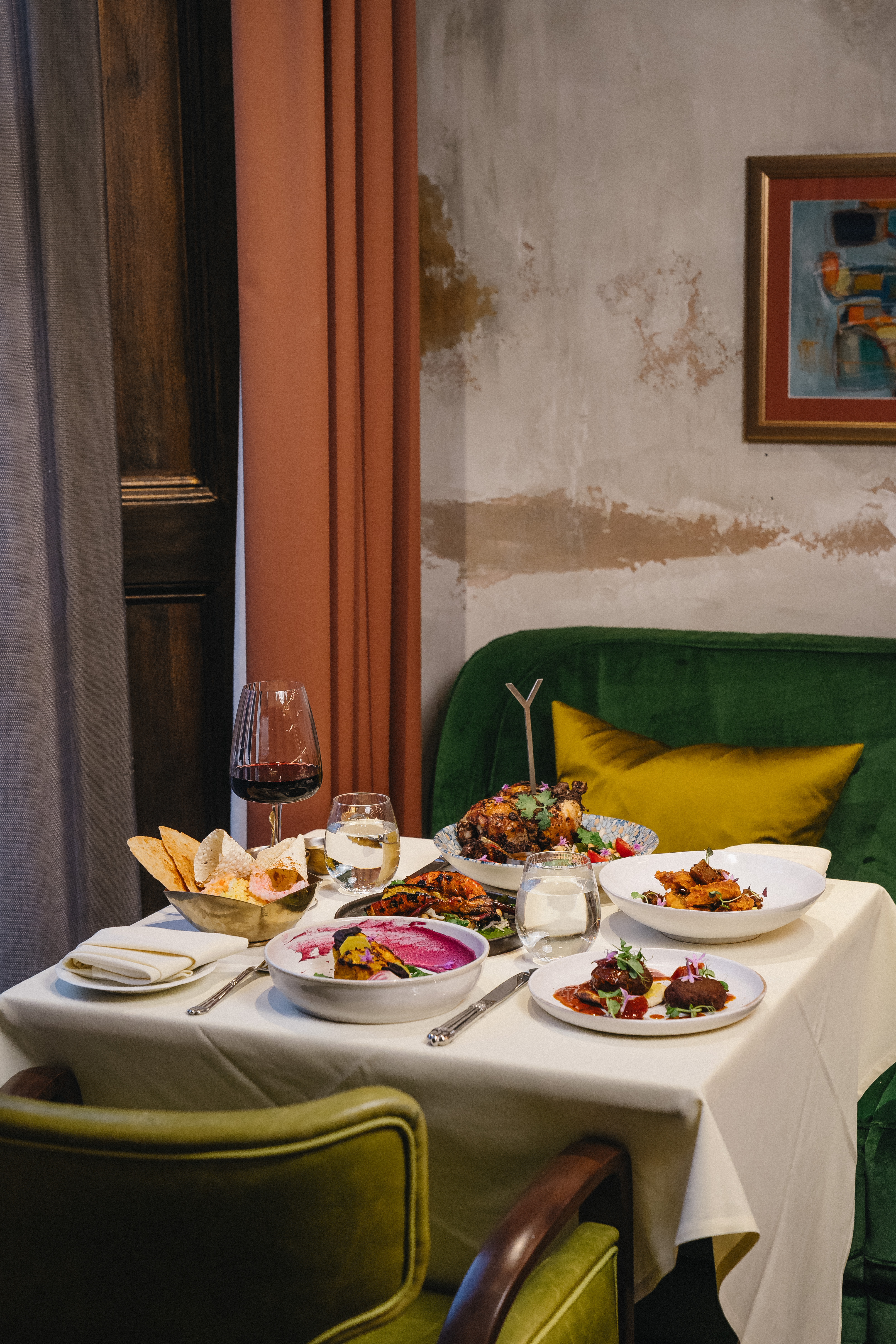 VATAVARAN - A selection of dishes on a table with a white tablecloth a green chair in the foreground and an orange curtain to its side