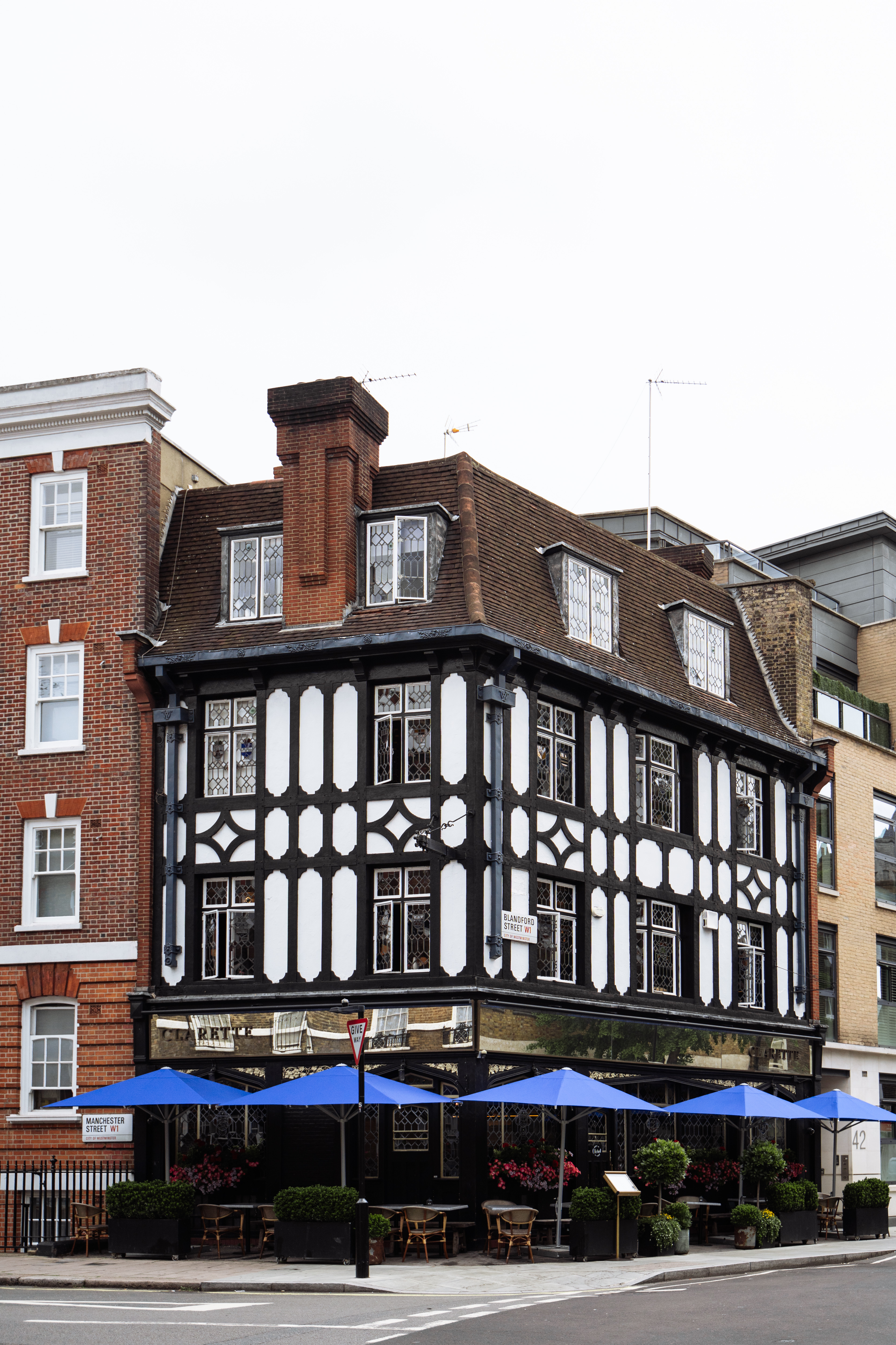 The exterior of Clarette, a luxury Tudor-style building with outdoor seating and blue umbrellas in Marylebone.
