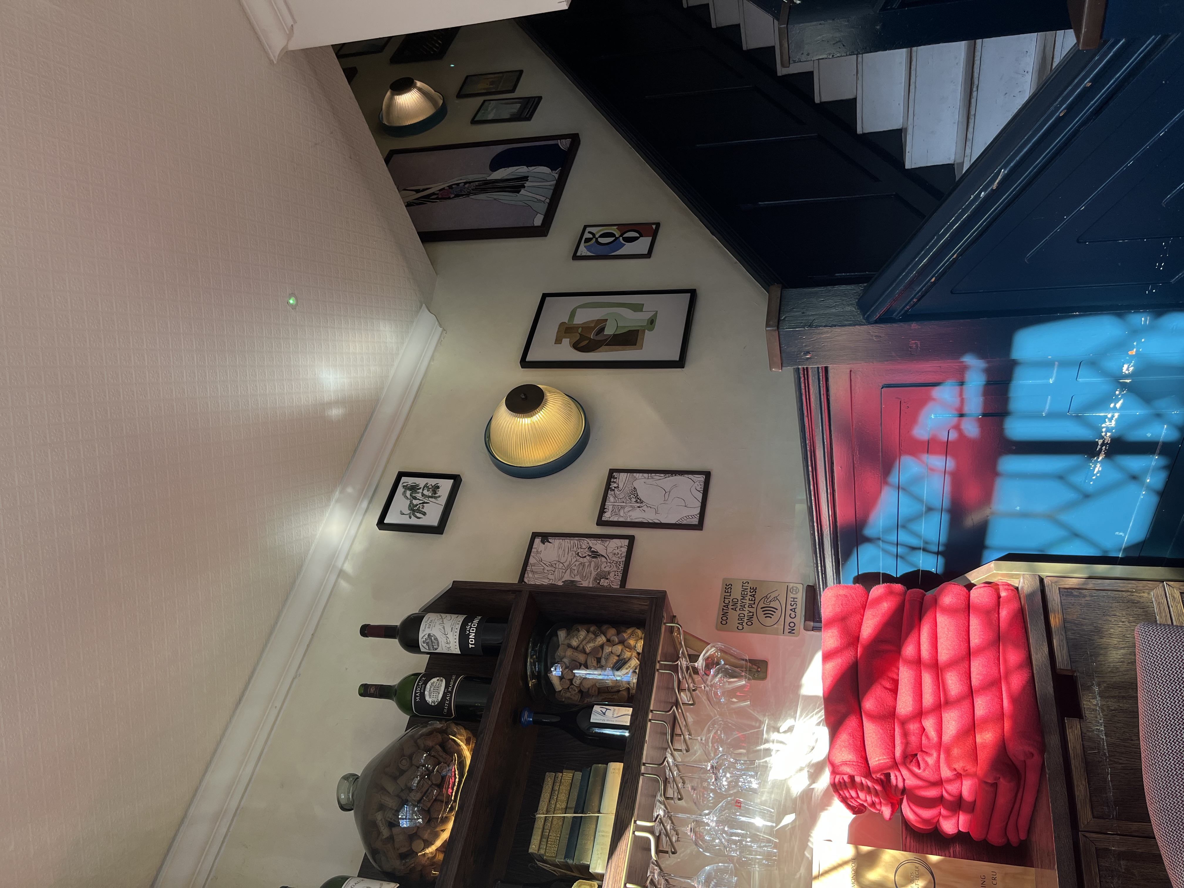 A cozy interior with framed artwork on the walls, a stack of red blankets, and a staircase.