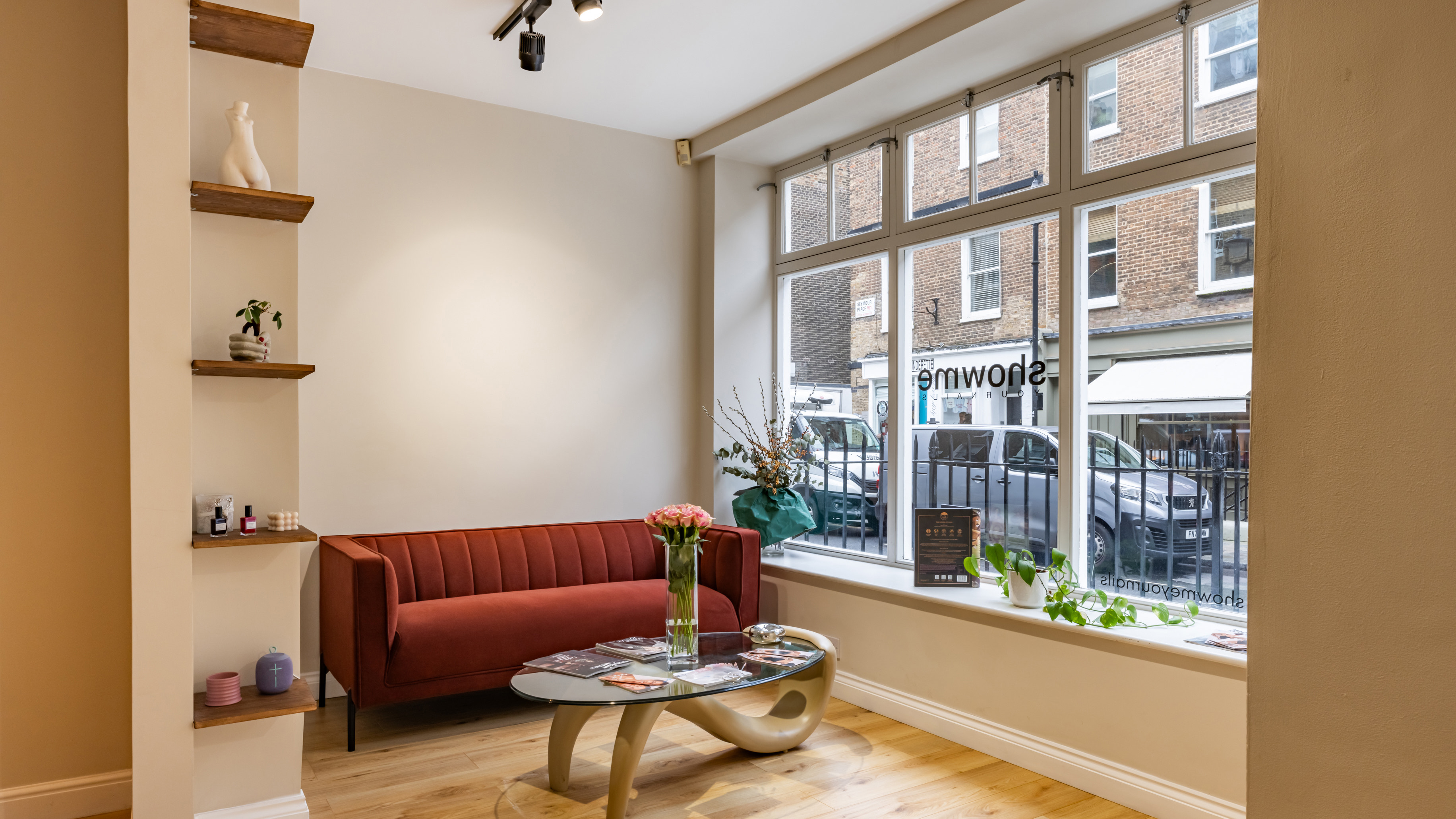 The modern interior of Show Me Your Nails salon in Marylebone with a red sofa, a glass coffee table, and shelves.