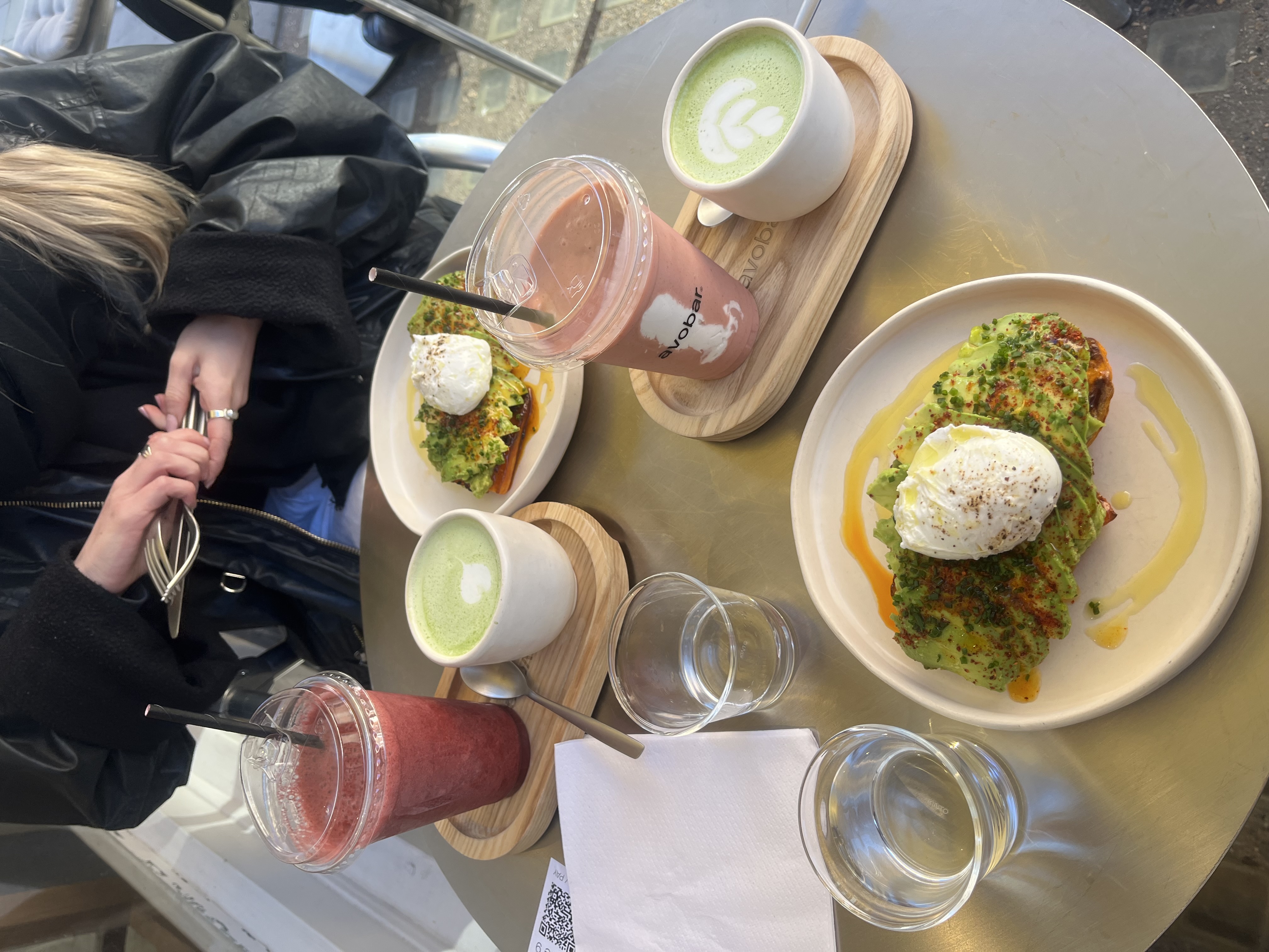 A table with two servings of avocado toast topped with a poached egg with cups of matcha and berry smoothies at avobar in Marylebone.