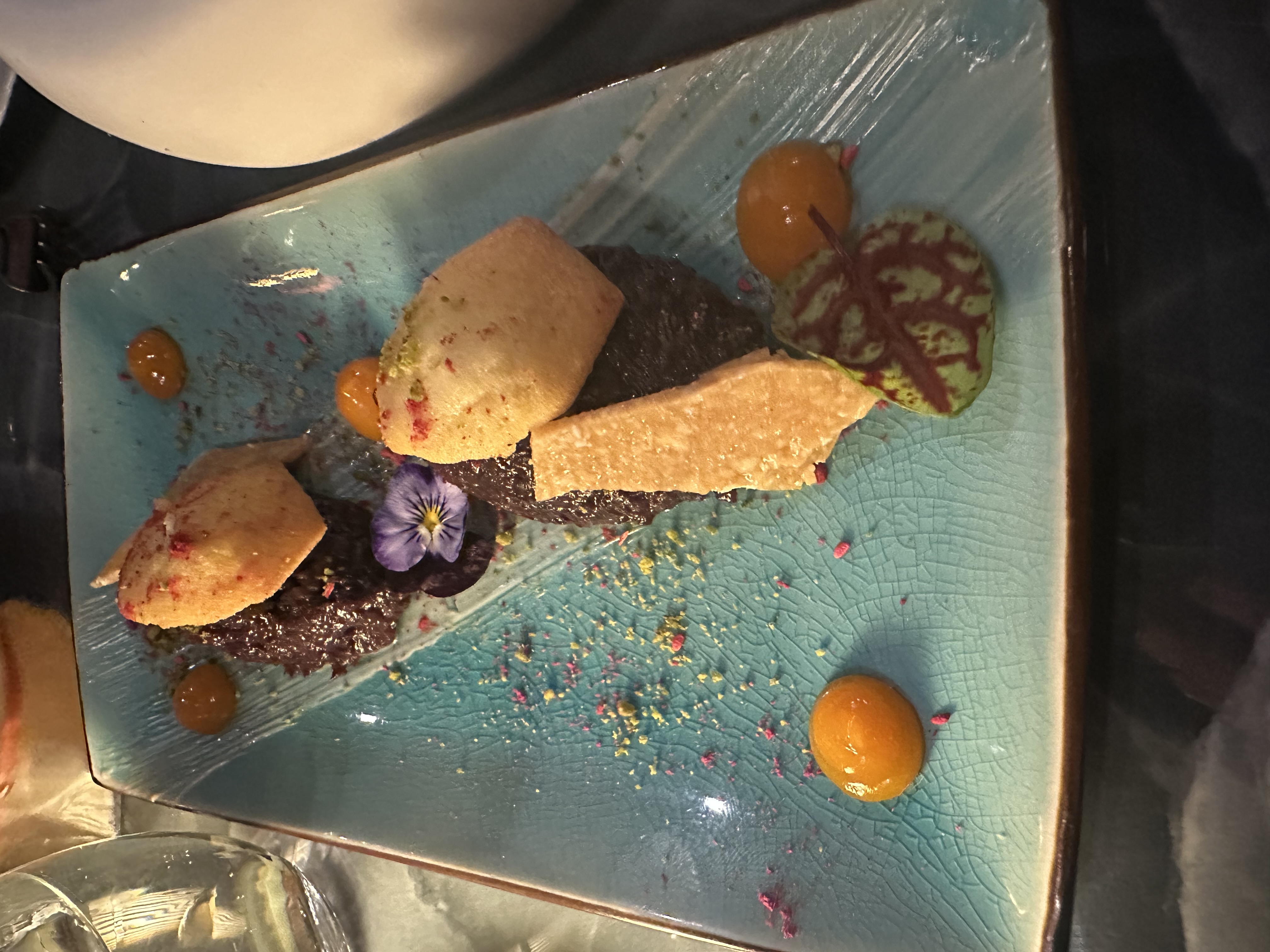 VATAVARAN - a biscuit dessert on a blue plate with orange dots of sauce and edible flowers