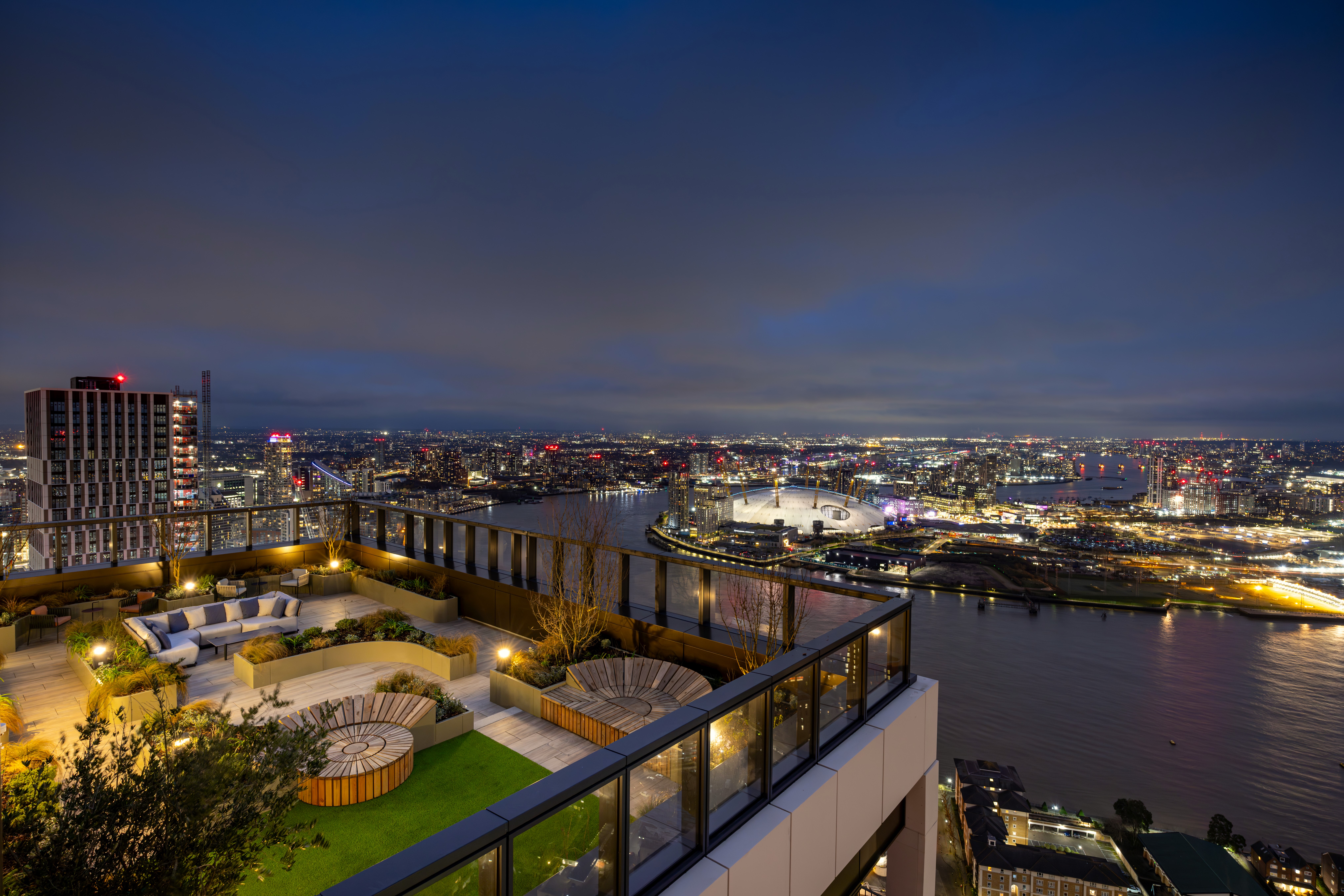Property of the Week One Thames Quay - A high-rise residential tower standing tall against a sunset-lit cityscape, surrounded by modern glass skyscrapers and waterways. The city's lights reflect off the buildings and water, capturing the vibrant energy of an urban skyline at dusk.