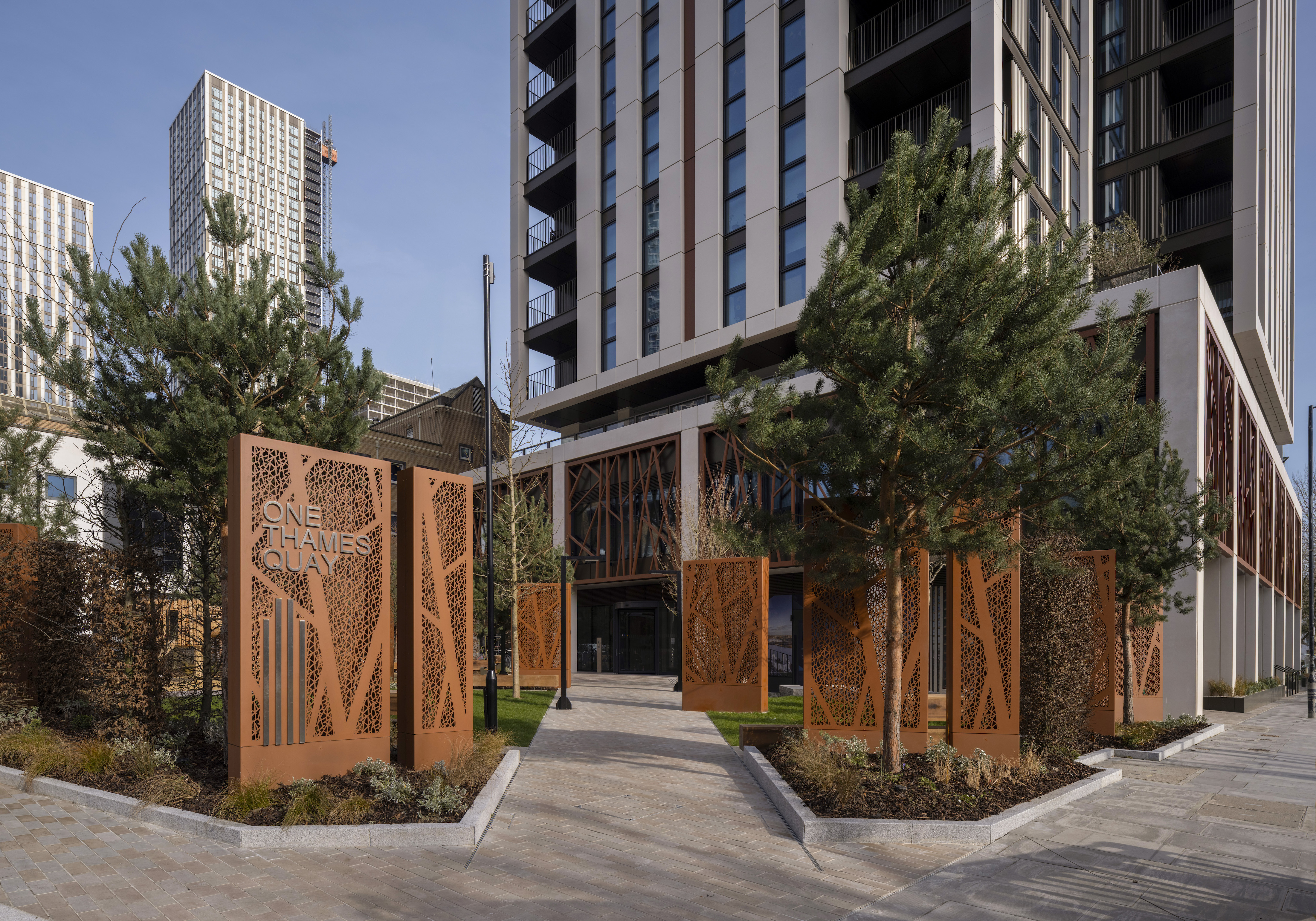 Property of the Week One Thames Quay - The entrance to One Thames Quay, featuring landscaped greenery, decorative rust-toned metal panels, and a modern high-rise tower with a sleek facade.