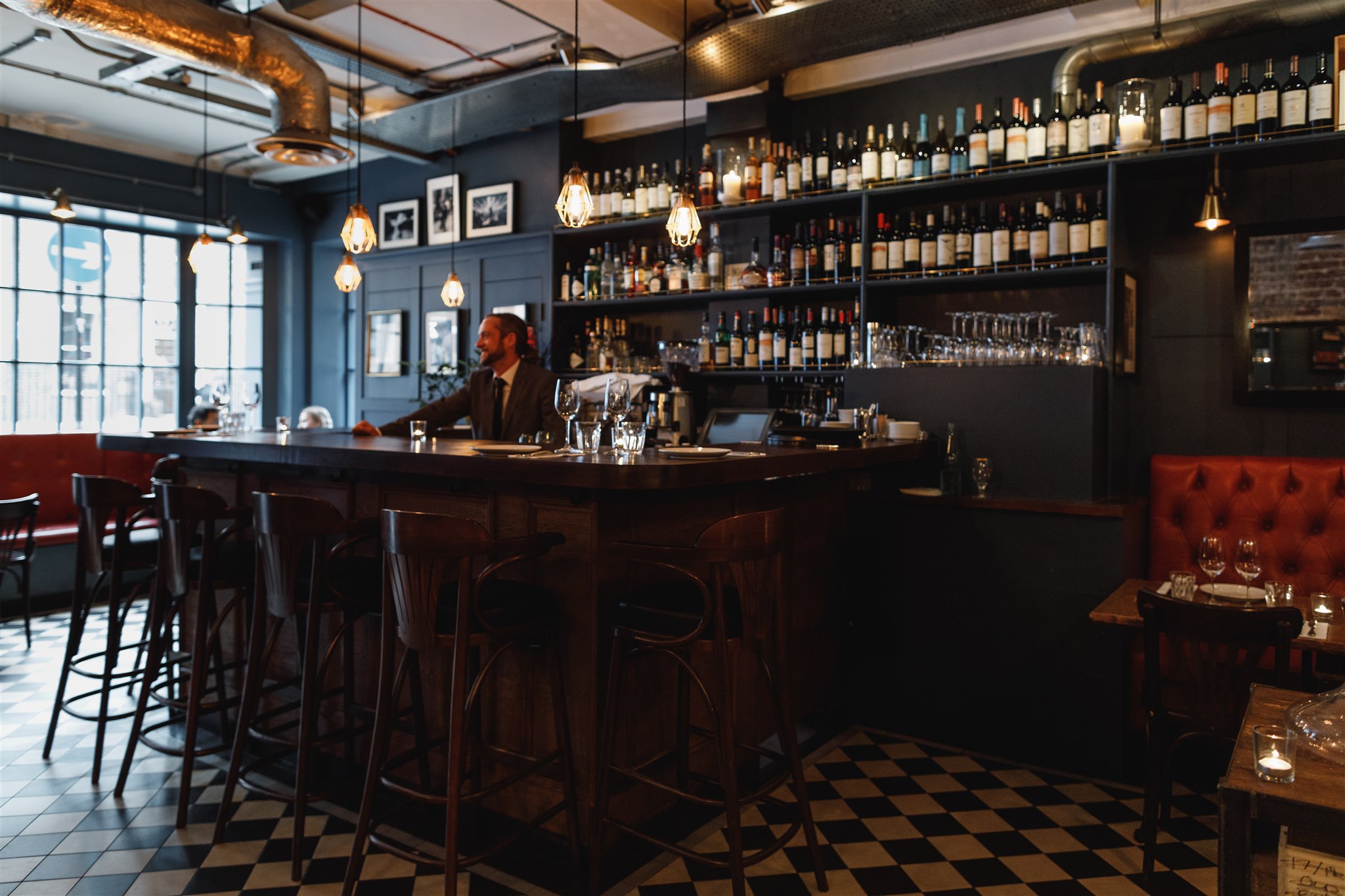 For your luxury 24 hours in Marylebone head inside ZOILO restaurant with a bar with wine shelves, a wooden counter, and a man in a suit at the bar.