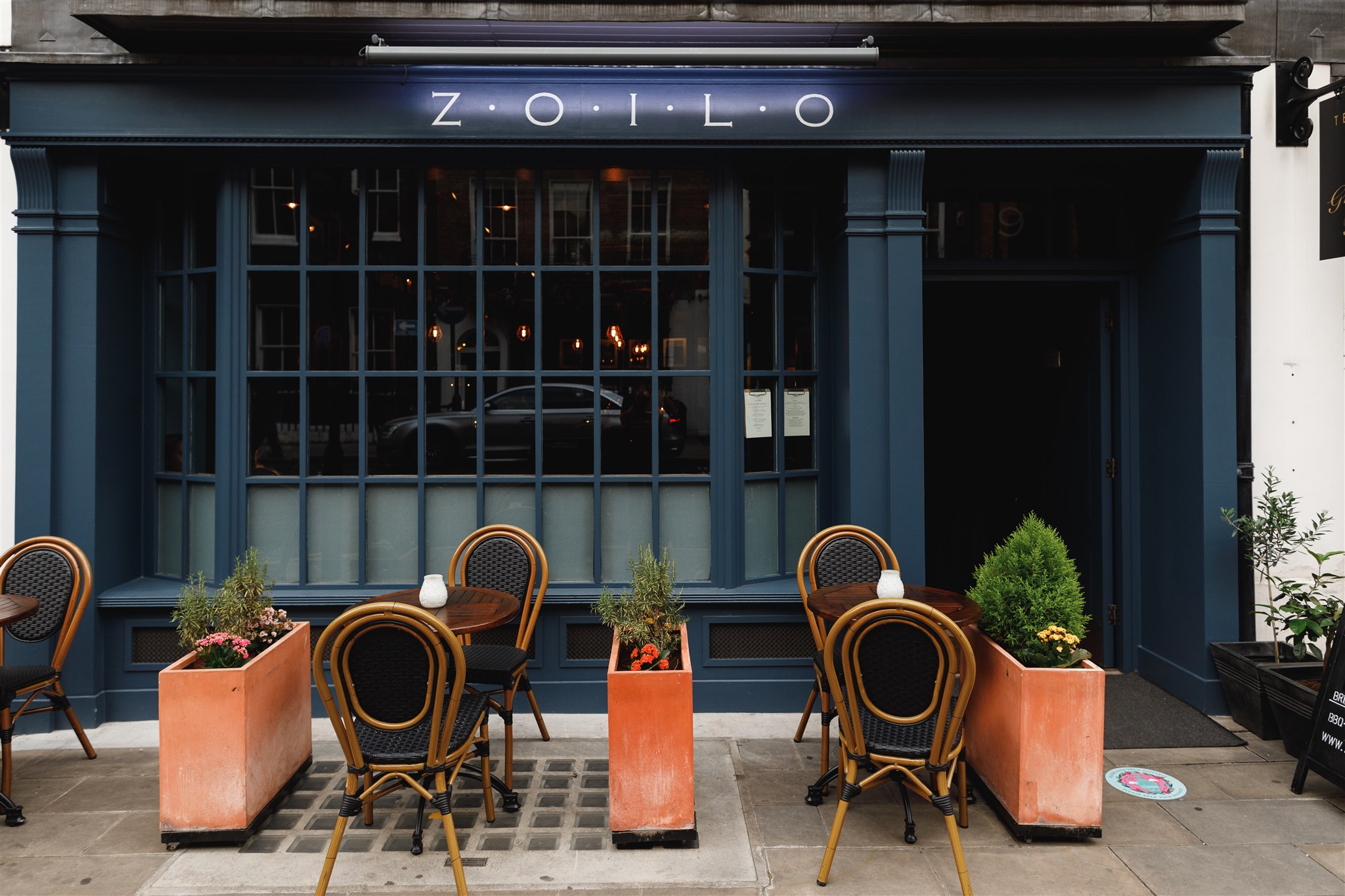 Outside ZOILO Restaurant on Blandford Street, the dinner location for your luxury 24 hours in Marylebone. With a navy blue exterior and potted flowers outside.