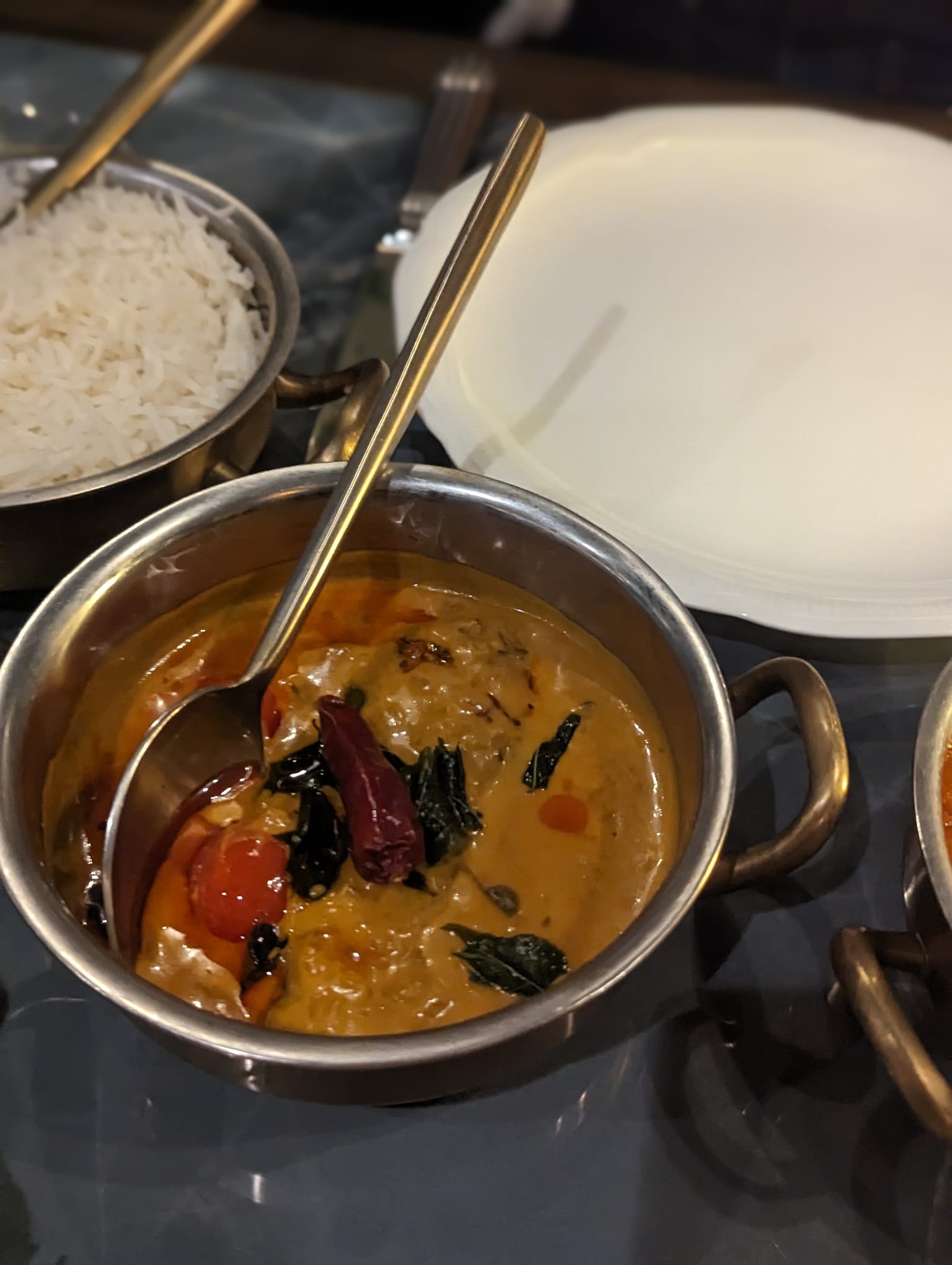 VATAVARAN- butter chicken curry in a silver pot alongside a white plate and a silver pot of white rice