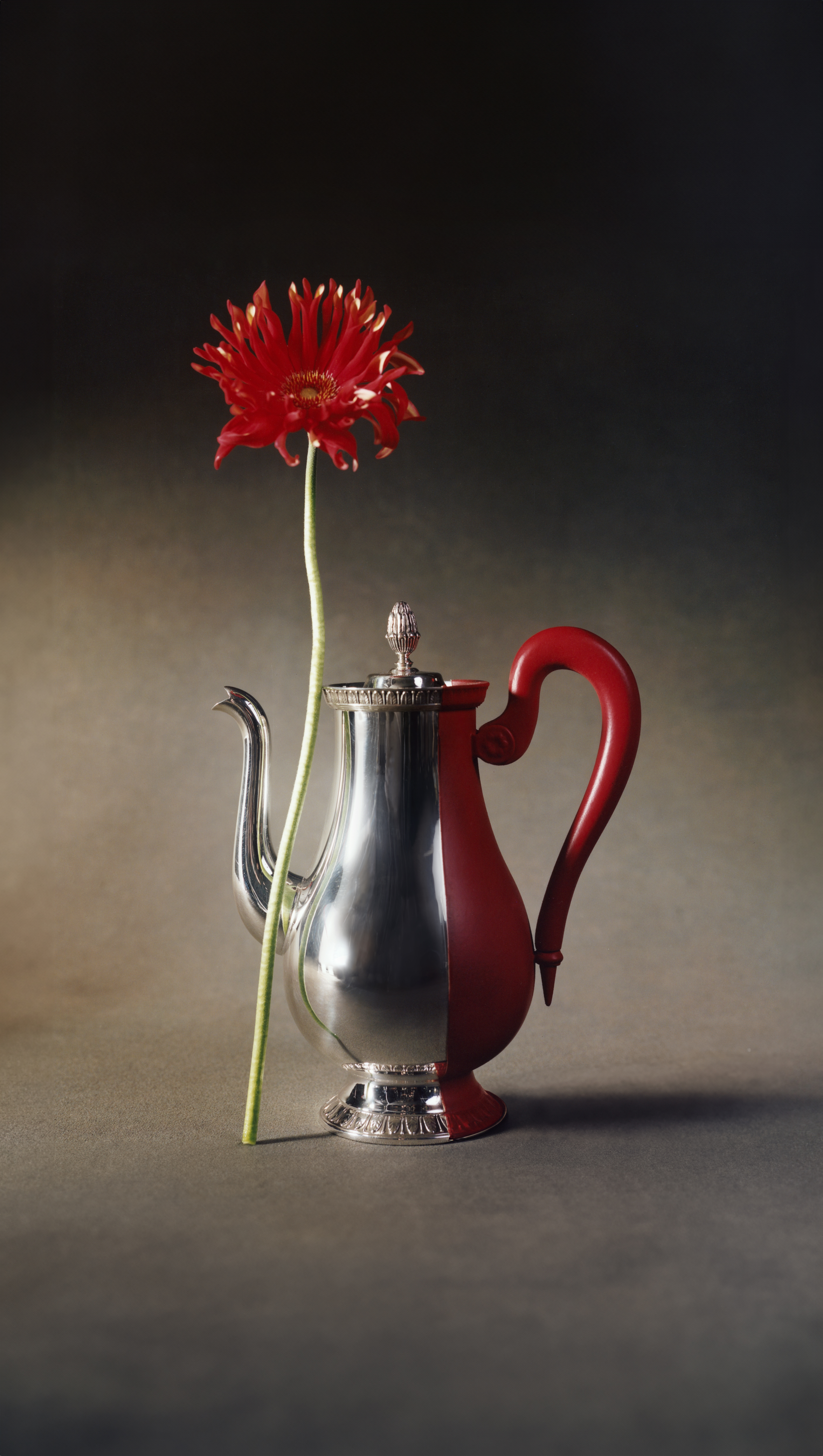 A silver and red Christofle Dip Malmaison coffee pot with a red flower emerging from its spout, displayed at the Christofle archive exhibition in Paris in 2025.