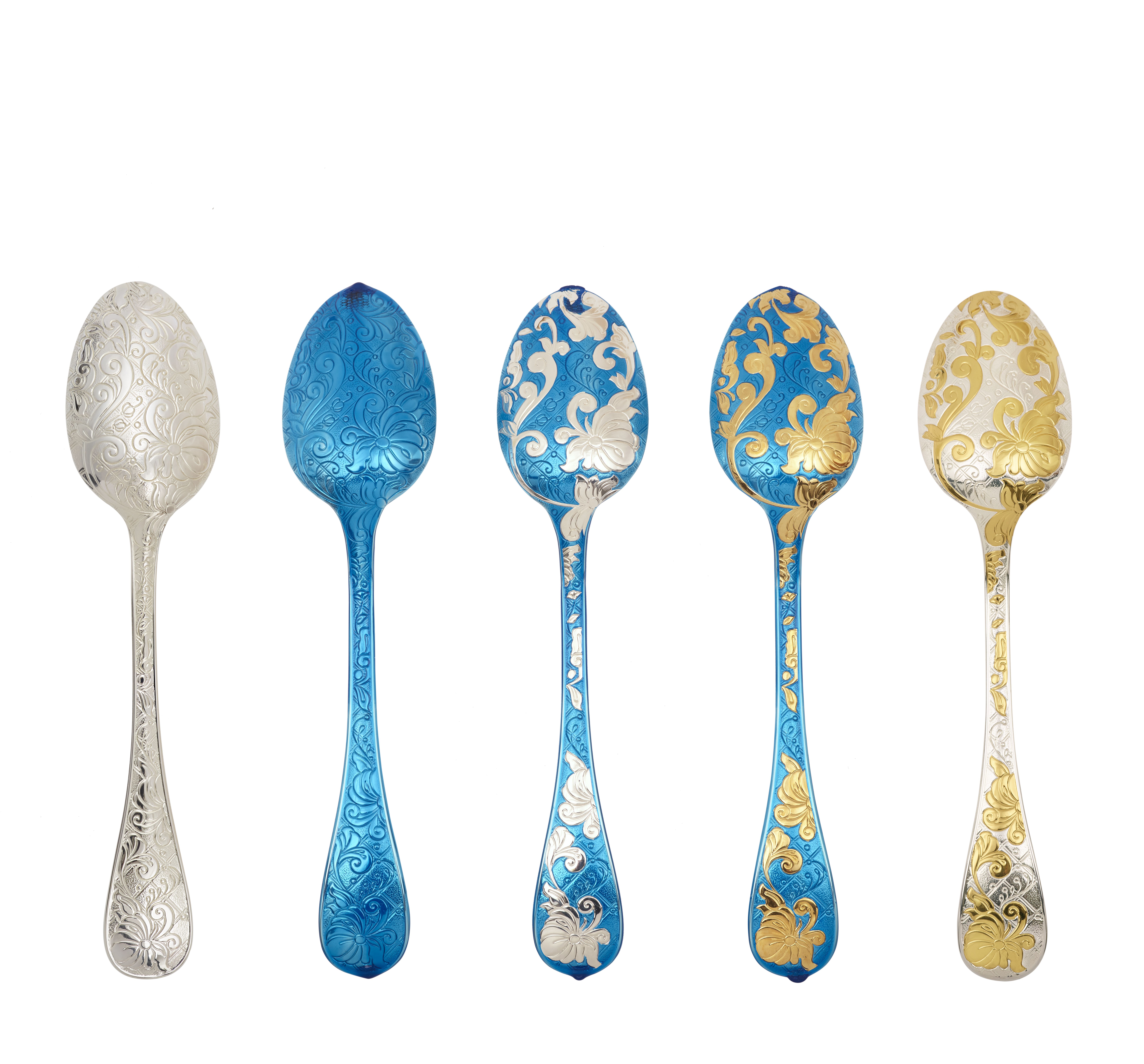 Five ornate Christofle spoons with intricate floral engravings in silver, blue, and gold at the Christofle Paris archive exhibition 2025.