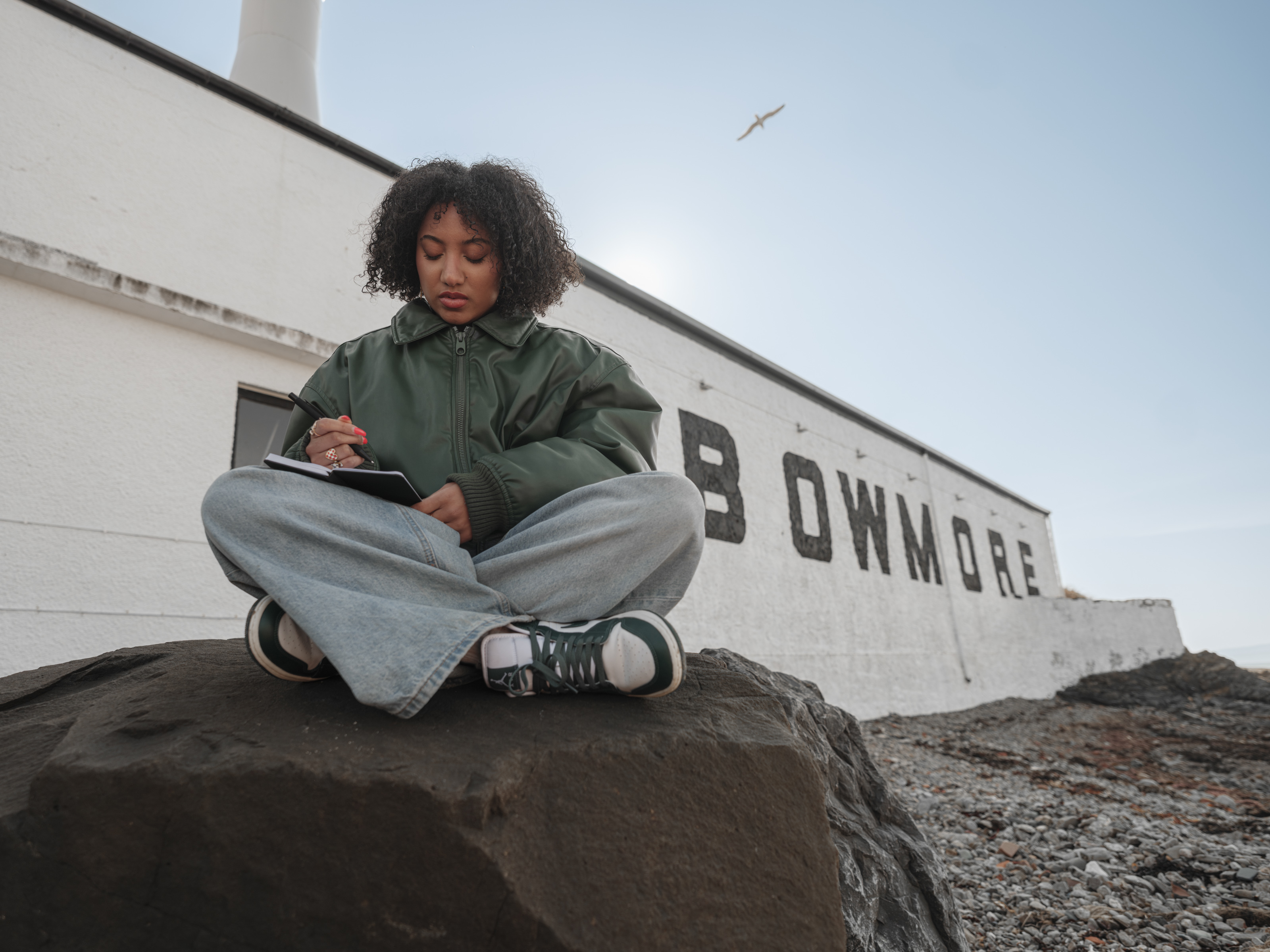 Sophia Thakur sat writing outside of the Bowmore Islay distillery 