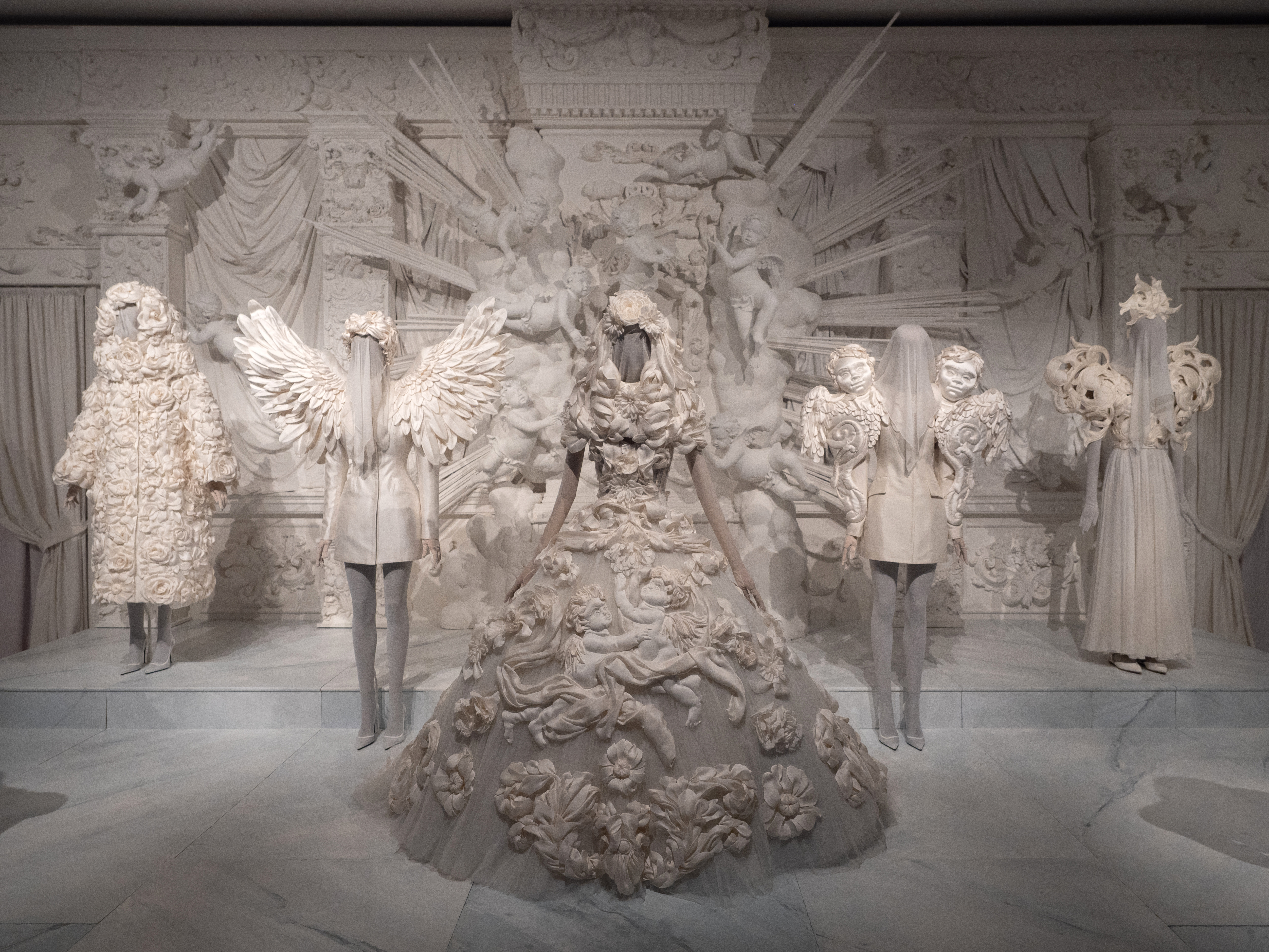 A display from the Dolce&Gabbana fashion archive exhibition in Paris featuring six intricately designed white ensembles on mannequins in Paris 2025.