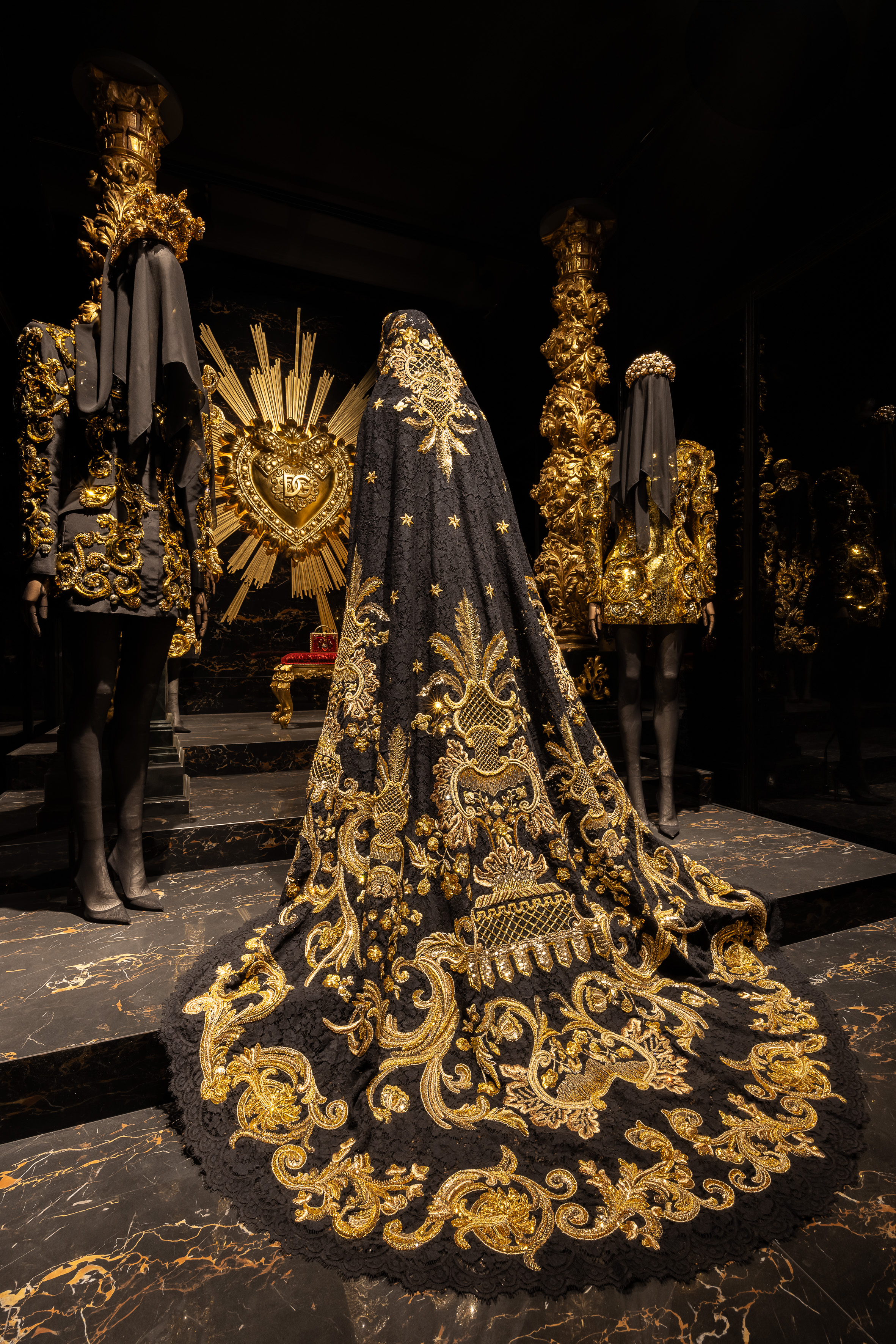 Baroque-inspired black and gold garments at the Dolce & Gabbana exhibition in Paris, with a central ornate gown featuring a sacred heart motif.