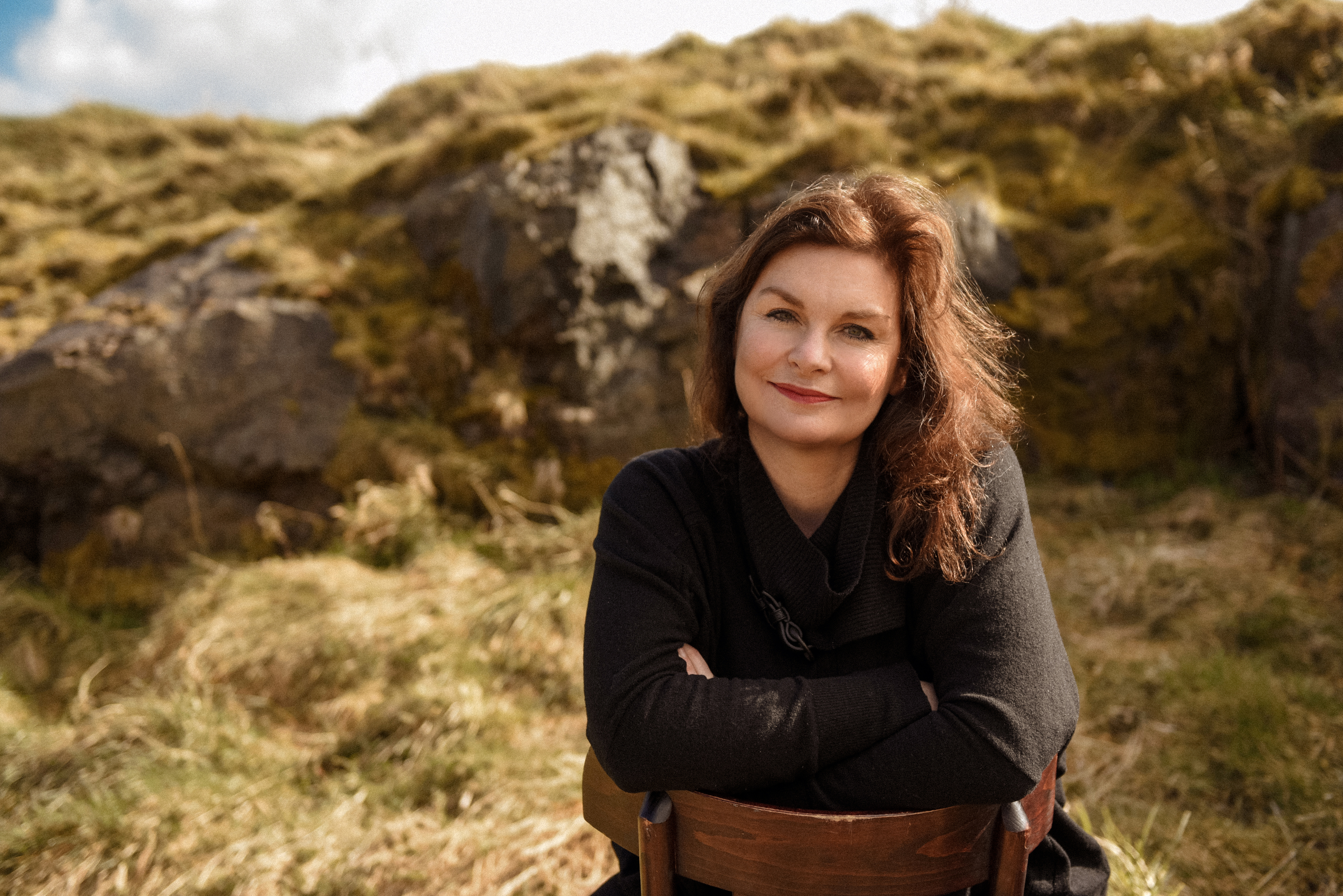 Imogen Russon-Taylor, the founder of luxury fragrance brand Kingdom Scotland, sitting outdoors in the Scottish landscape.