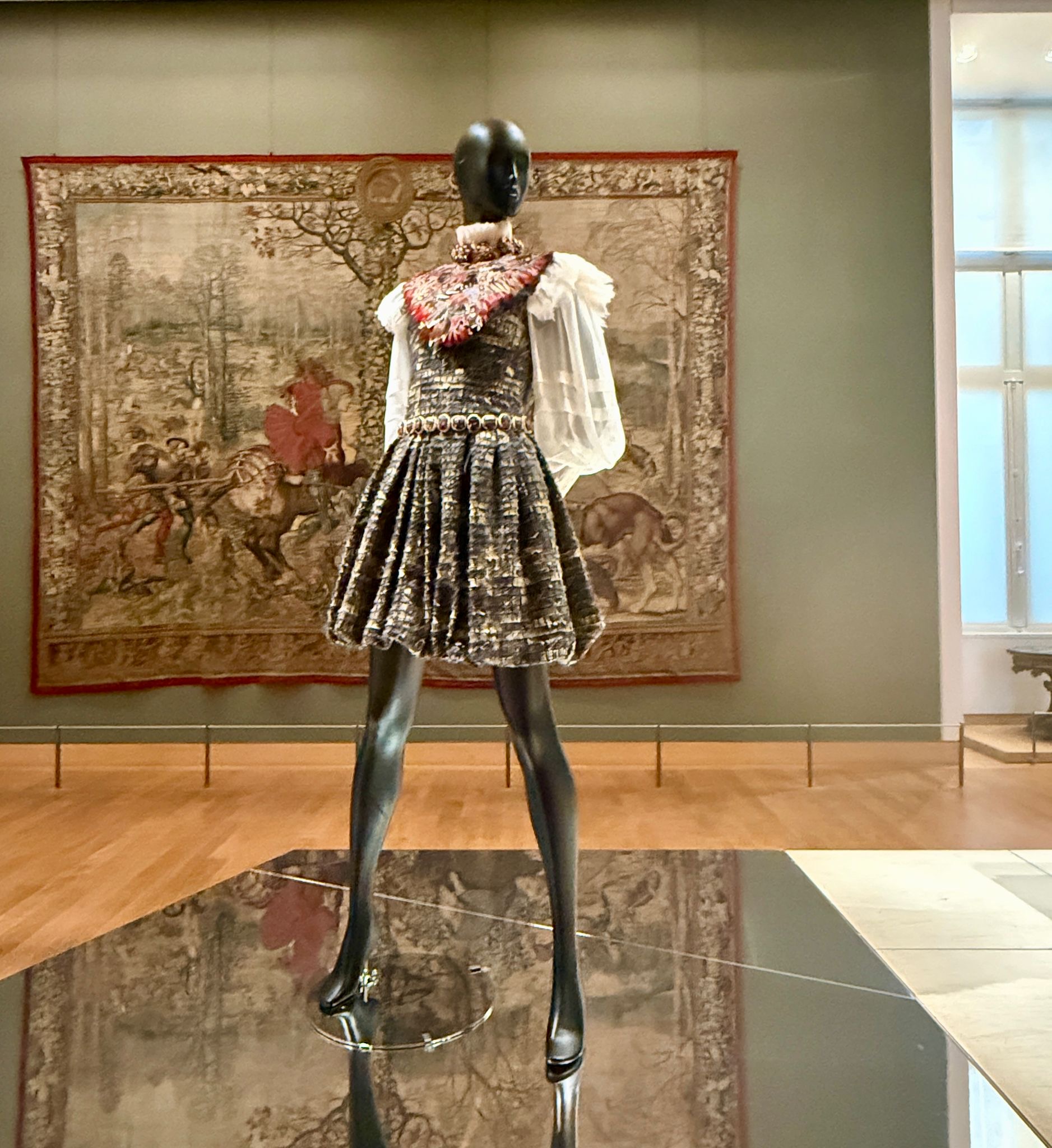 A mini dress with a full skirt, white sheer puffed sleeves, and an elaborate red and gold collar by Chanel, displayed at the Louvre Couture exhibition in 2025.