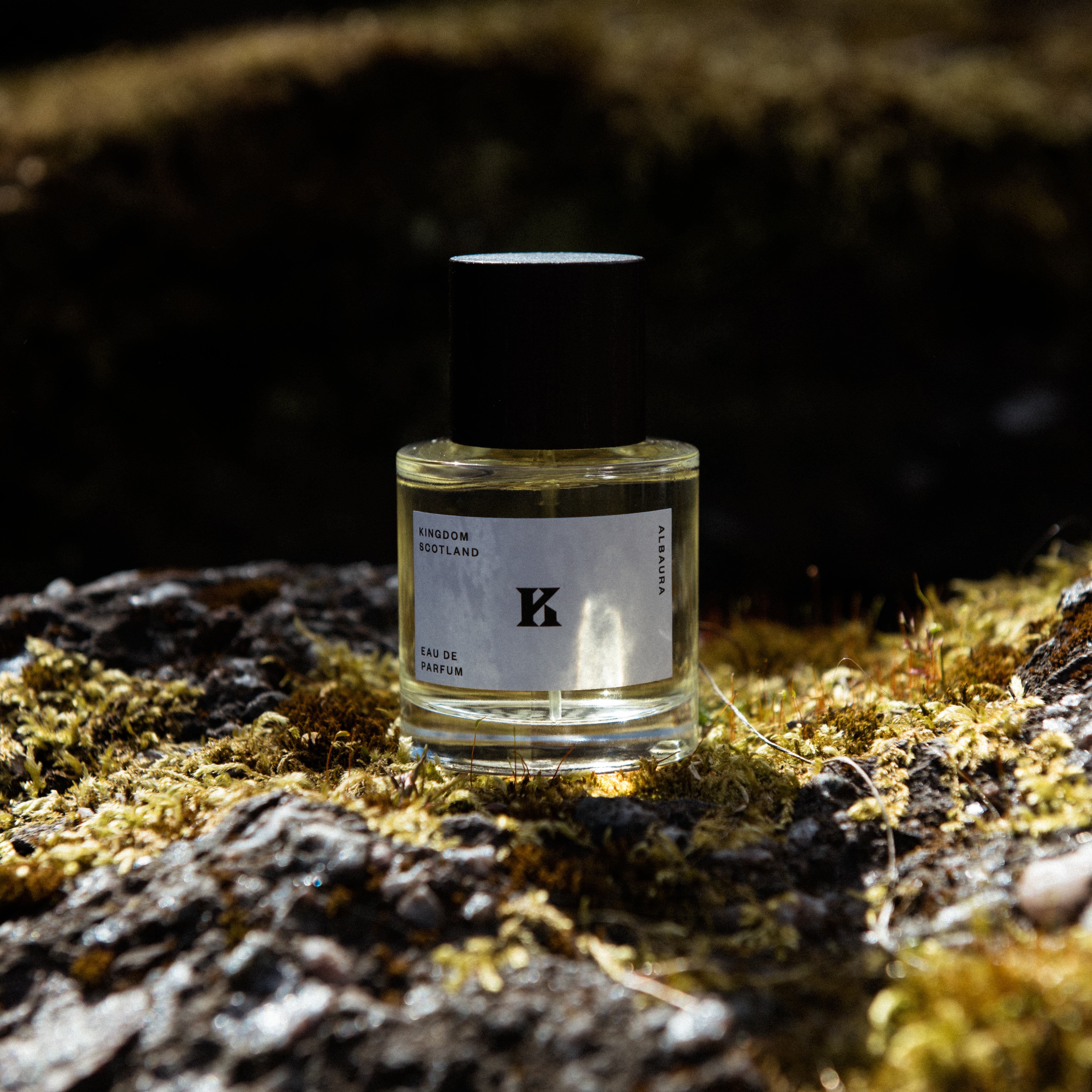 A luxury fragrance bottle of Albaura by Kingdom Scotland sitting on a moss covered rock.