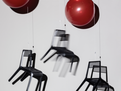 A selection of lightweight chairs drift away, tied to a pair of red balloons. 