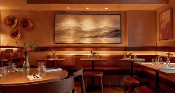 Art restaurants in London - warmly lit restaurant interior of Lolo in Bermondsey featuring wooden tables and cushioned bench seating. A large framed landscape painting serves as the focal point.